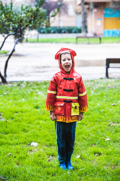 Chłopiec przebrany za strażaka w czerwonym płaszczu rozpryskuje się na trawie - Zdjęcie, obraz