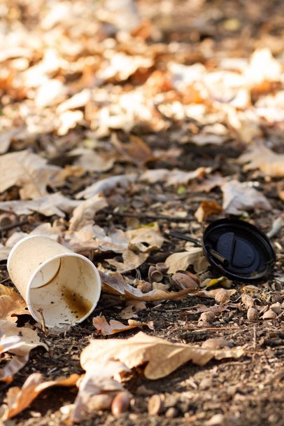 Paper coffee cup with plastic lid on the ground. Discarded disposable coffee cup with a plastic lid. Empty single use paper coffee cup - 写真・画像