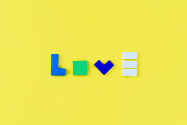 Слово "LOVE" зроблено з різнокольорових дерев'яних цеглин на жовтому тлі. Вид зверху, плоский ліжко
. - Фото, зображення