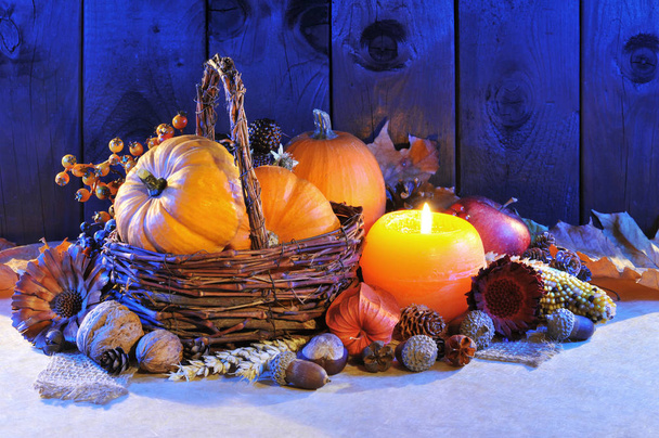 thanksgiving - various squashes,nuts,corn and apple in rattan basket with candlelight in blue evening light\n - Фото, изображение
