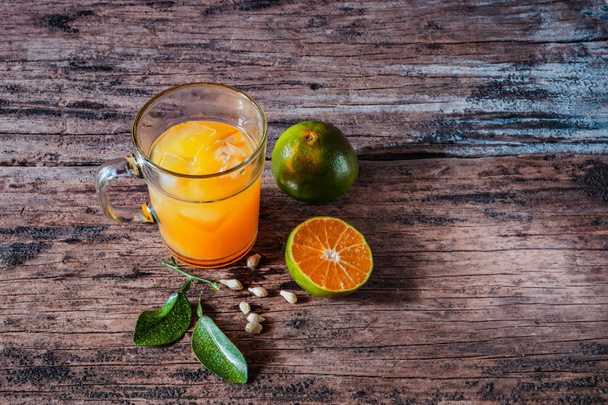 Стакан апельсинового сока на старинном деревянном столе, дополненный ломтиками свежих местных апельсинов и их листьями. В Индонезии этот напиток называется jus jeruk
. - Фото, изображение