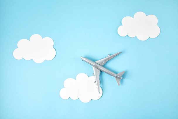 Miniature airplane over blue background with paper clouds. Travel tourism, airlines, low cost flights concept. Top view, flat lay. - Foto, immagini
