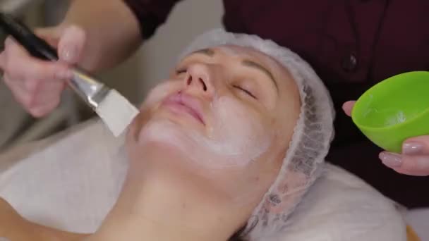 Professional cosmetologist woman puts a mask on the face of the patient. - Footage, Video
