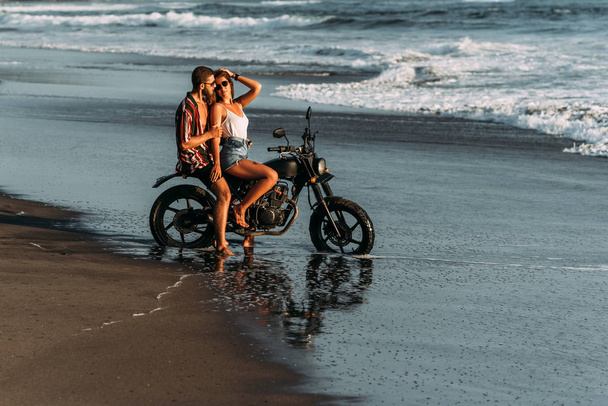 A couple in love on the beach meets the sunset. Beautiful couple on a motorbike meets sunset by the sea. Man and woman are traveling on a motorbike in Bali. Man and woman at sunset. Vacation at sea - Foto, immagini