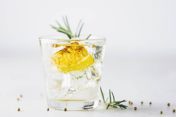De gebrande citroen, rozemarijn en koriander gin en tonic zijn perfect uitgebalanceerde verfrissende cocktails. op lichte achtergrond, close-up. Zomerdrankjes en alcoholische of detox cocktail - Foto, afbeelding