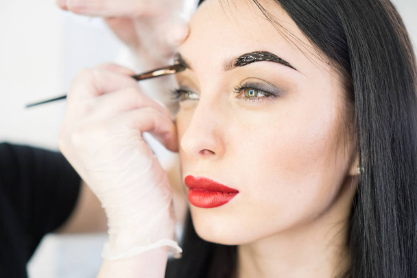 Beautiful woman in a beauty salon. Eyebrow correction process close-up.  - Photo, Image