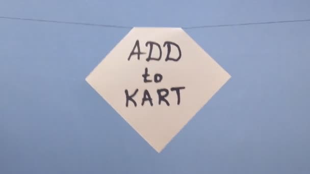 Een man hangt een wit vel papier met een zwarte inscriptie "add to kart" op een blauwe achtergrond - Video