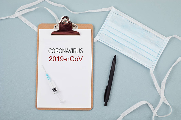 Coronavirus 2019-nCoV text on clipboard, disposable medical mask, personal protective equipment, syringe filled medicine or vaccine and medicine pills. Virus concept - Valokuva, kuva