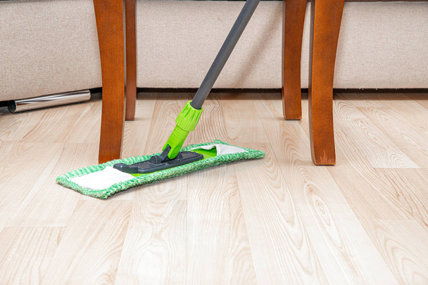 Limpiando el suelo con una fregona. El concepto de cuidado para la limpieza del apartamento. El hombre limpia el suelo con una fregona verde. Un hombre limpiando el apartamento
. - Foto, Imagen