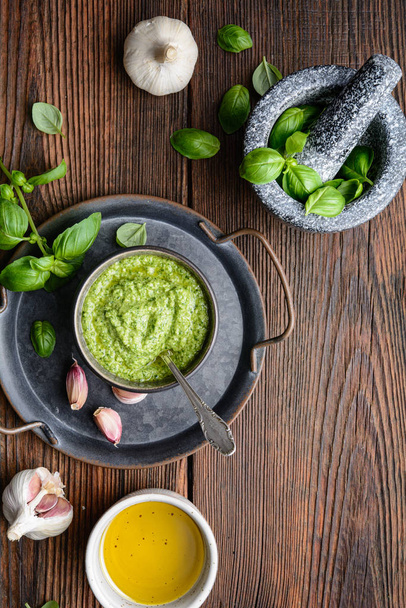 Homemade fresh basil pesto sauce in a bowl, decorated with leaves, garlic and mortar with copy space - Foto, Imagen