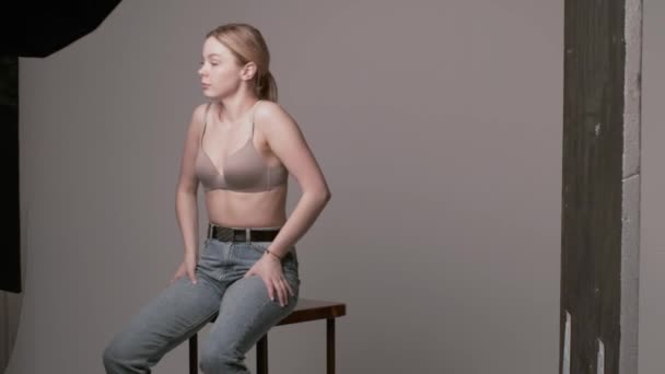backstage van sexy meisje poseren in beige beha, jeans op witte studio achtergrond - Video