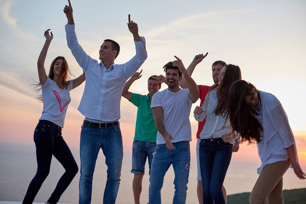 group of happy young people dancing and have fun on party in modern home bacony with sunset and ocean in background - Valokuva, kuva