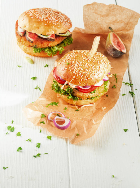 High Angle View of Two Vegetarian Couscous Burgers with Fresh Toppings and Herbs on Sesame Seed Rolls with Onion Slices on Brown Paper Wrapper with Copy Space - Фото, изображение
