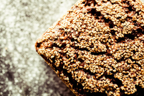 High Angle View of Artisinal Whole Grain Bread with Cracked Crust Surface and Covered with Sesame Seeds on Flour Covered Surface with Copy Space - Photo, image