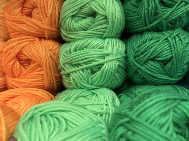 Texture of different sharpness from tangles of yarn in orange and green shades laid out in vertical rows. Mobile photo with store lighting. - Photo, image