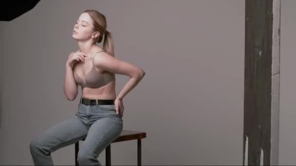 backstage van Kaukasisch meisje met lang haar poserend in beige beha, jeans in studio - Video