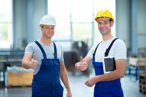 Zwei junge Arbeiter mit erhobenem Daumen in Fabrik - Foto, Bild