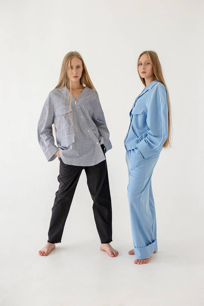 two pretty young twin sistersposing on white background in oversize clothes - Foto, afbeelding