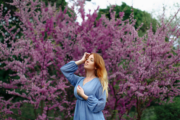 Beautiful dreaming redhead woman in spring time blossom cherrytrees garden. - 写真・画像