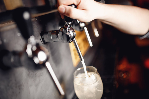 Dark background, Barman pours light alcoholic cider of keg tap into glass - Photo, Image