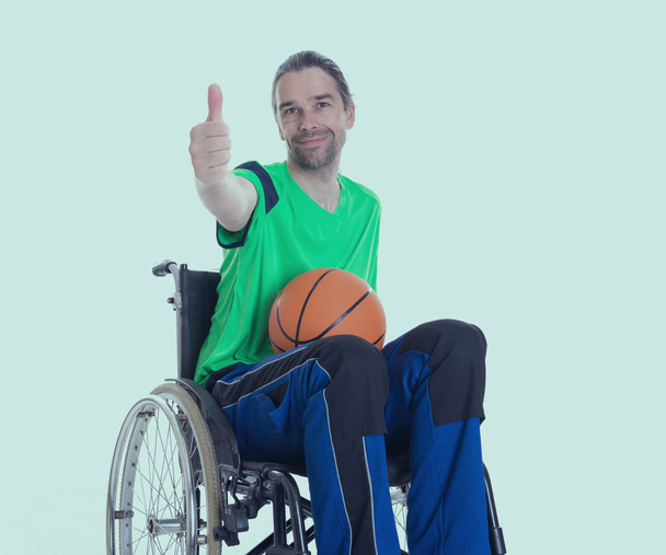 mladý zdravotně postižený muž na invalidním vozíku dělá sport s míčem a palcem nahoru - Fotografie, Obrázek