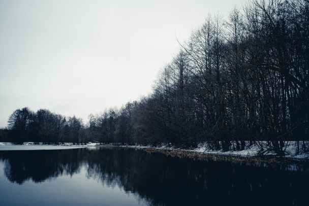 Calm pond on cold winter day. Peaceful lake water and snowy coast on cold gray day in winter countryside - Foto, immagini