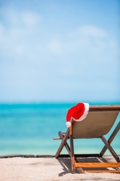 Sun loungers with Santa Hat at beautiful tropical beach with white sand and turquoise water. Perfect Christmas vacation - Photo, Image