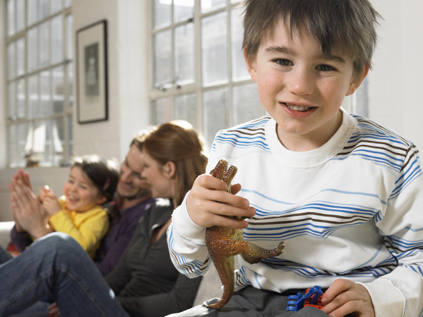 Boy holding toy dinosaur in living room, (portrait) - Fotoğraf, Görsel