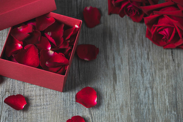 Confezione regalo rossa con petali di rosa dentro e rose rosse
 - Foto, immagini
