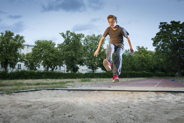 side view full length shot of a male young teenager frozen while jumping into a long jump pit - Foto, imagen