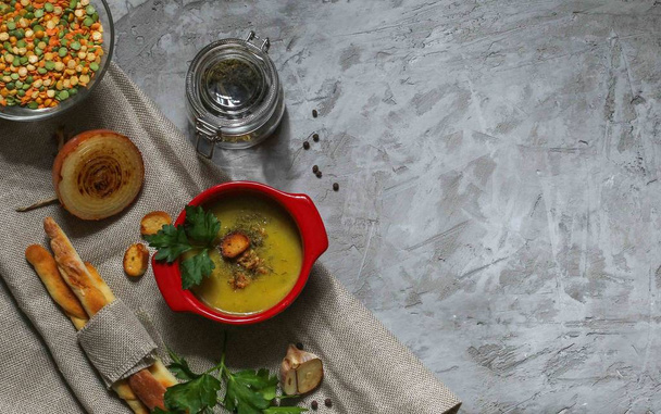 вегетарианский кремовый бобовый суп в красной кастрюле и хлебные палочки на льняной салфетке на сером фоне с видом на пространство сверху
 - Фото, изображение