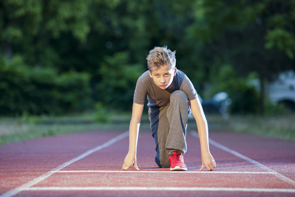 deep front full body view of a young male teenager looking in depth starting position on a tartan track in the camera - Foto, Bild