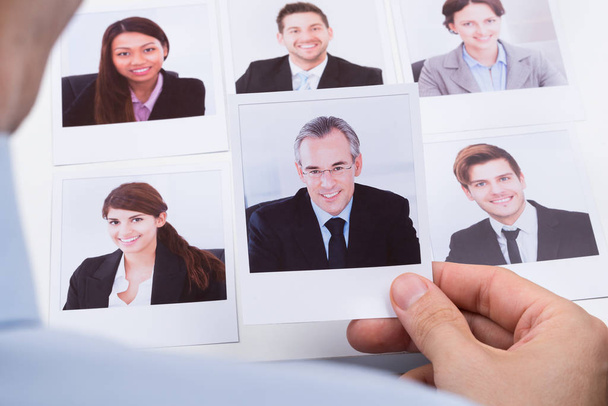 Close-up Of Businessperson Choosing Photograph Of Best Job Candidate - Photo, image