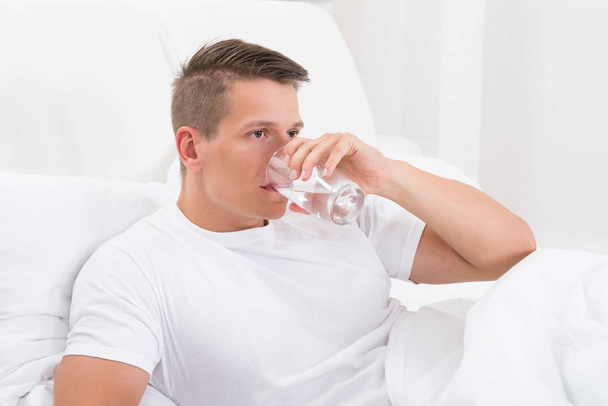 Young Man Sitting In Bed Drinking Water - Foto, Imagen