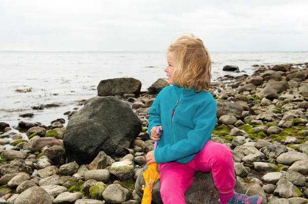 little girl on stone beach is looking to the sea - Foto, afbeelding