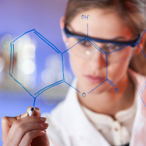 Kendine güvenen bir kadın sağlık uzmanının portresi çalışma ortamında cam bir tahtaya yapısal kimyasal formül yazıyor.. - Fotoğraf, Görsel