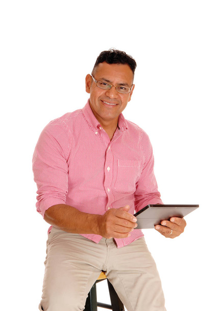 A Hispanic man sitting on a chair with glasses working on his tablet.computer, isolated for white background.. - Zdjęcie, obraz