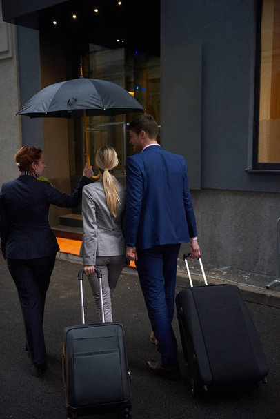 Young business people couple entering city  hotel, looking for room, holding suitcases while walking on street - Foto, Imagen
