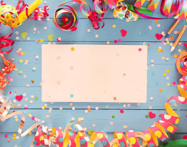 Διακοσμητικό πλαίσιο κόμμα πολύχρωμα σερπαντίνες σπιράλ και κομφετί πάνω από ένα ρουστίκ φόντο μπλε ξύλο με κεντρική λευκή κάρτα με copyspace για χαιρετισμό ή πρόσκλησή σας - Φωτογραφία, εικόνα
