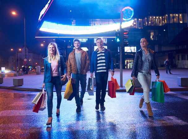 Group Of Friends Enjoying Shopping Trip Together.group of happy young frineds enjoying shopping night and walking on steet on night in with mall in background - Photo, image