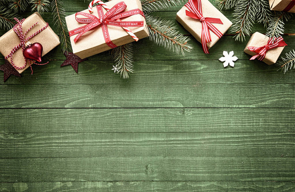 Rustic festive Christmas border with gift-wrapped presents tied with colorful red ribbon amongst fresh pine foliage across the top of the frame over green wood with copyspace - 写真・画像