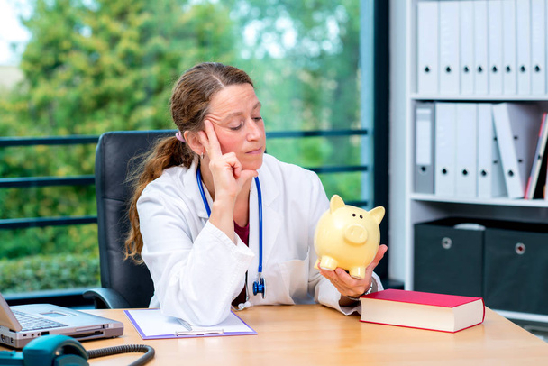 young female doctor in her office with a piggy bank - Foto, immagini