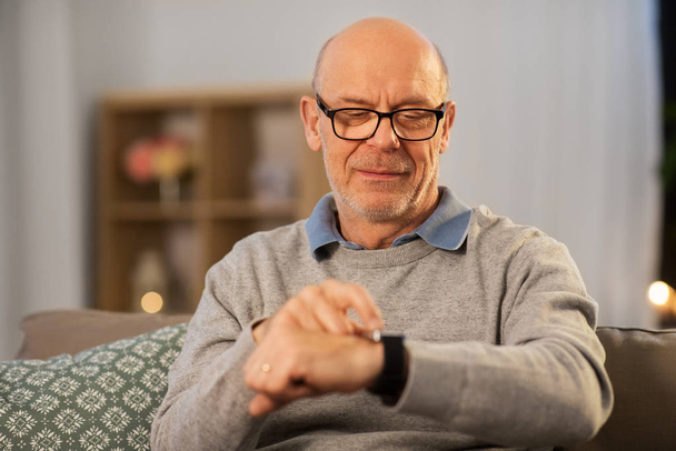 senior man looking at wristwatch at home - Foto, Bild