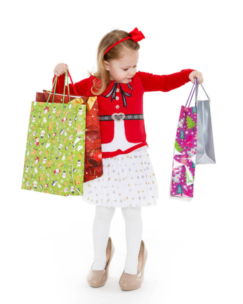 Happy pretty little child with shopping bags stands on a white background. 3 year old. - 写真・画像
