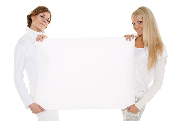 Two young pretty women in winter clothes with empty board for the text on a white background. - 写真・画像
