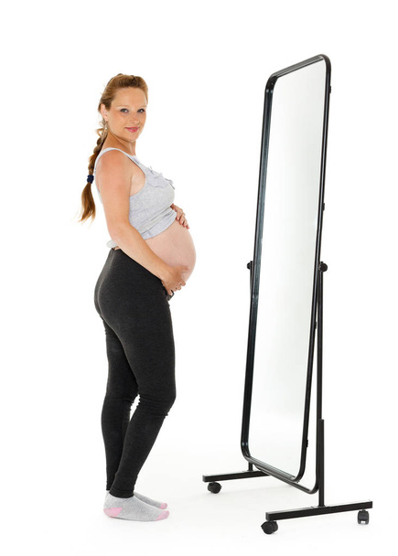 Pregnant woman stands before mirror on a white background. - Foto, Bild