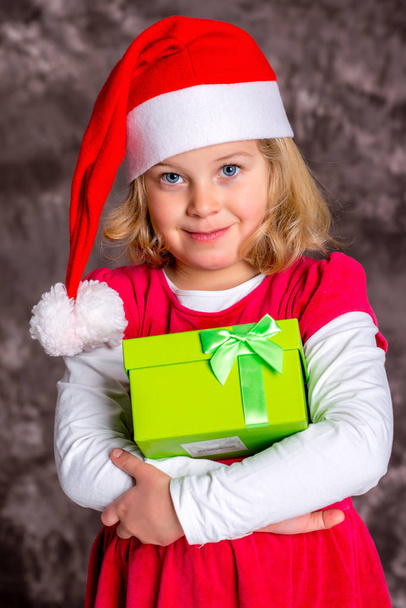 kleines Mädchen mit Santa- Mütze und Geschenk - Foto, Bild