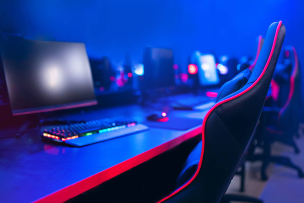 Рабочее место для профессионального геймера в компьютерных играх, онлайн-турнирах, удобном кресле, подсветке клавиатуры, мониторах, синем и красном фоне
 - Фото, изображение