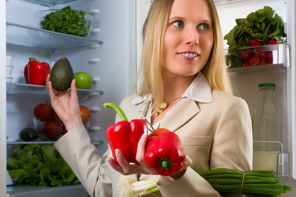 Attractive business woman showing vegetables for healthy eating in front of a refrigerator - Foto, Imagen
