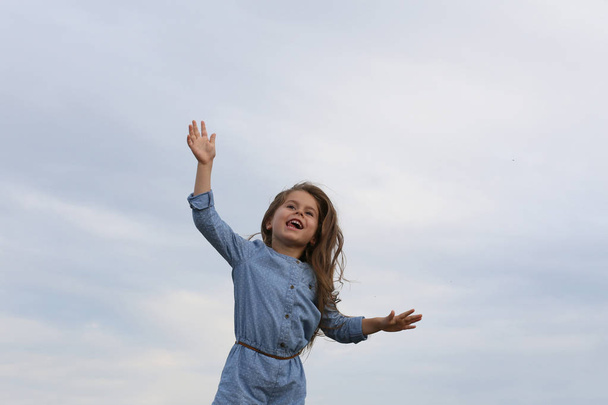 šestiletá dívka v modrém oblečení smích s pažemi široce otevřené a - Fotografie, Obrázek